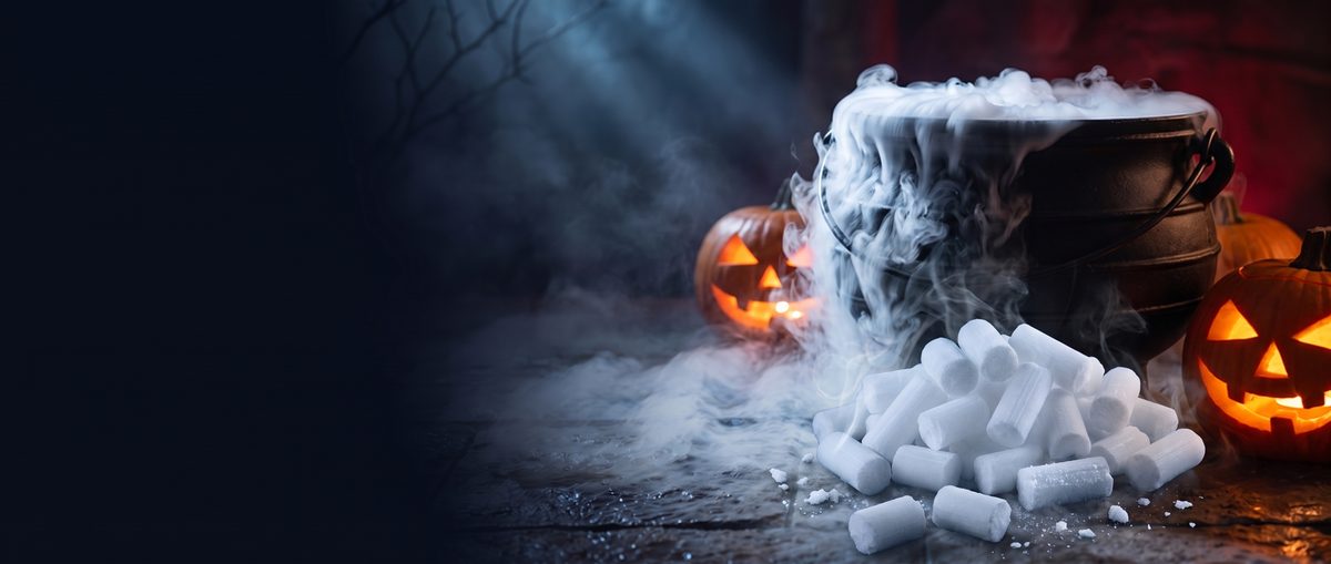 A pile of 16 mm dry ice nuggets in front of a cauldron spilling fog, with two carved pumpkins glowing